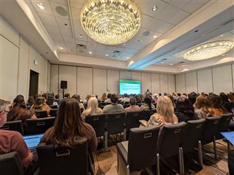 Two women presenting a powerpoint in a room of participants at a conference.