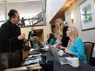 Two women speaking at an event registration table. 