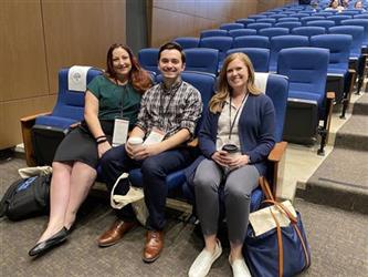 Three symposium participants sitting and smiling in their seat in the main auditorium.