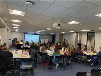 Groups sitting at tables in a large room listening to a presentation.