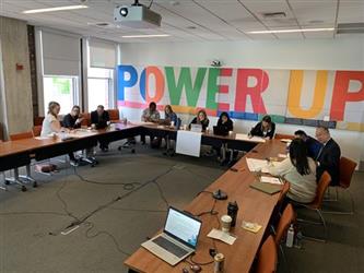 Group of people sitting at long tables and talking during a lunch and learn meeting. 