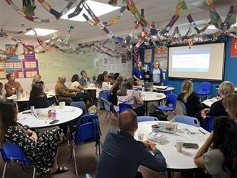 Groups sitting at round tables in a classroom listening to a presentation.